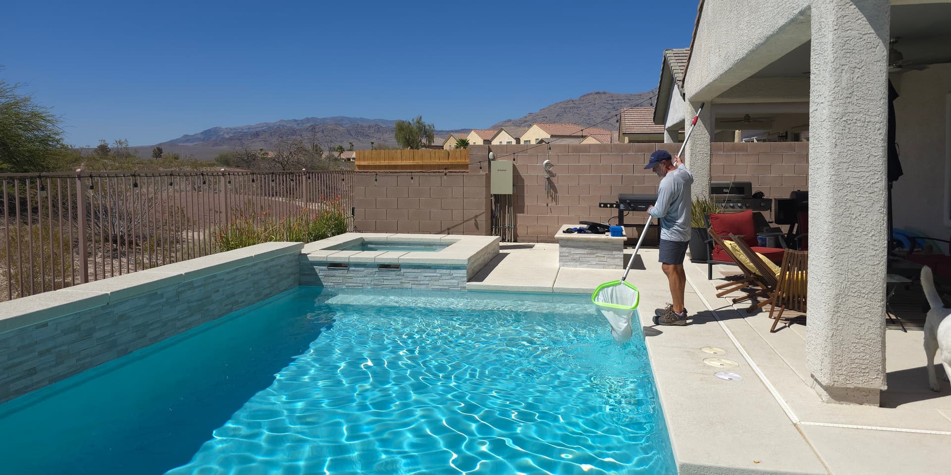 Michael Brown, AquaVision Pool Care owner and Certified Pool Operator, skimming a residential pool and spa with a Las Vegas Valley desert and mountain backdrop